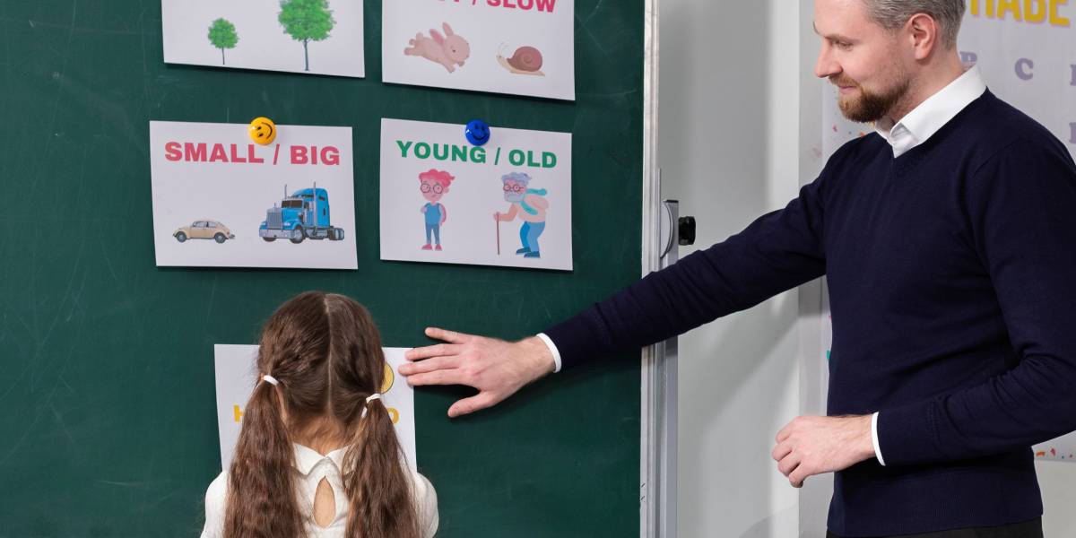 Niño en el aula con dificultades para expresarse verbalmente, acompañado por una docente que lo apoya, reflejando una situación de aprendizaje afectado por el lenguaje.
